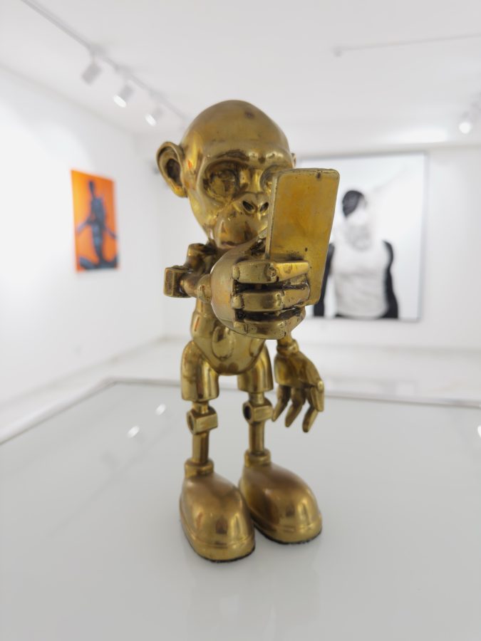 Toy Art by Beto Gatti, polished golden bronze sculpture of a primate-headed figure with robotic joints and oversized shoes staring at a smartphone, 2022